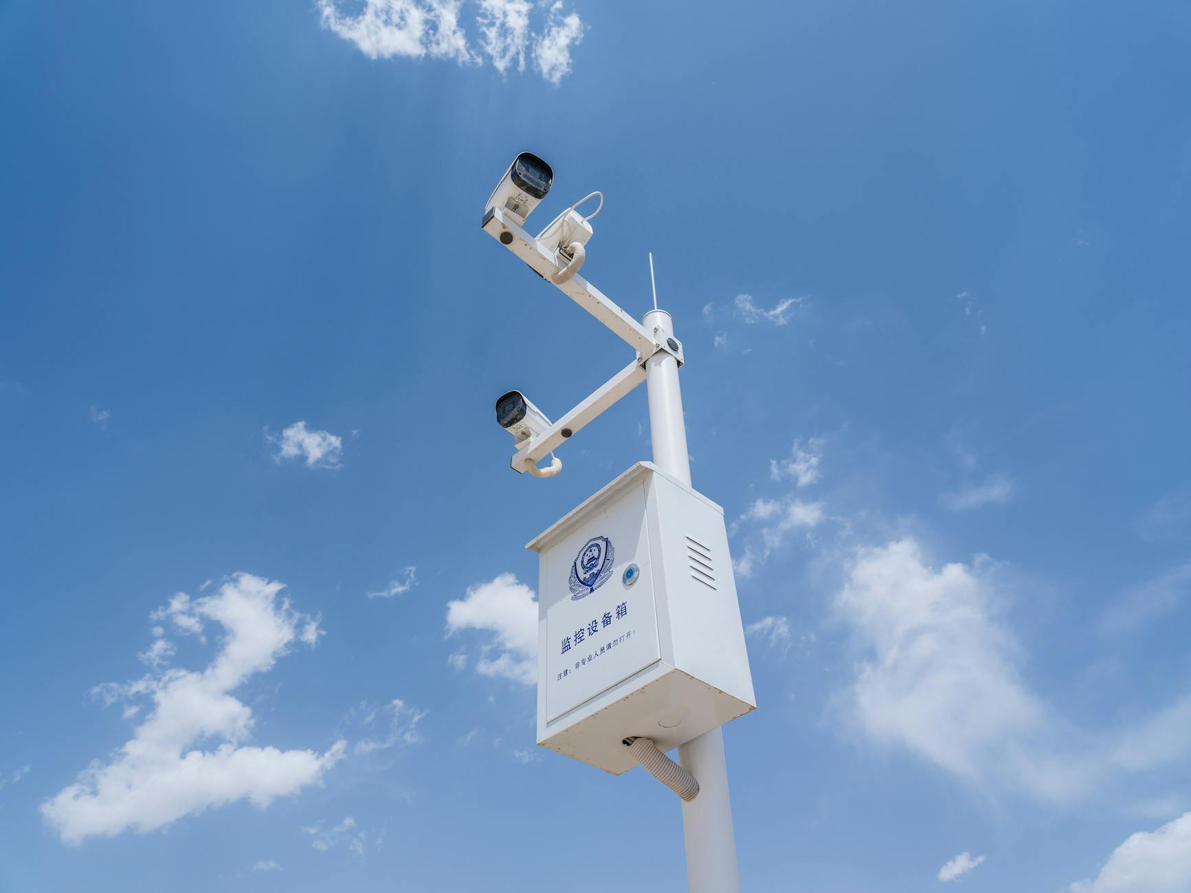 Białe kamery monitoringu na słupie na tle nieba z chmurami