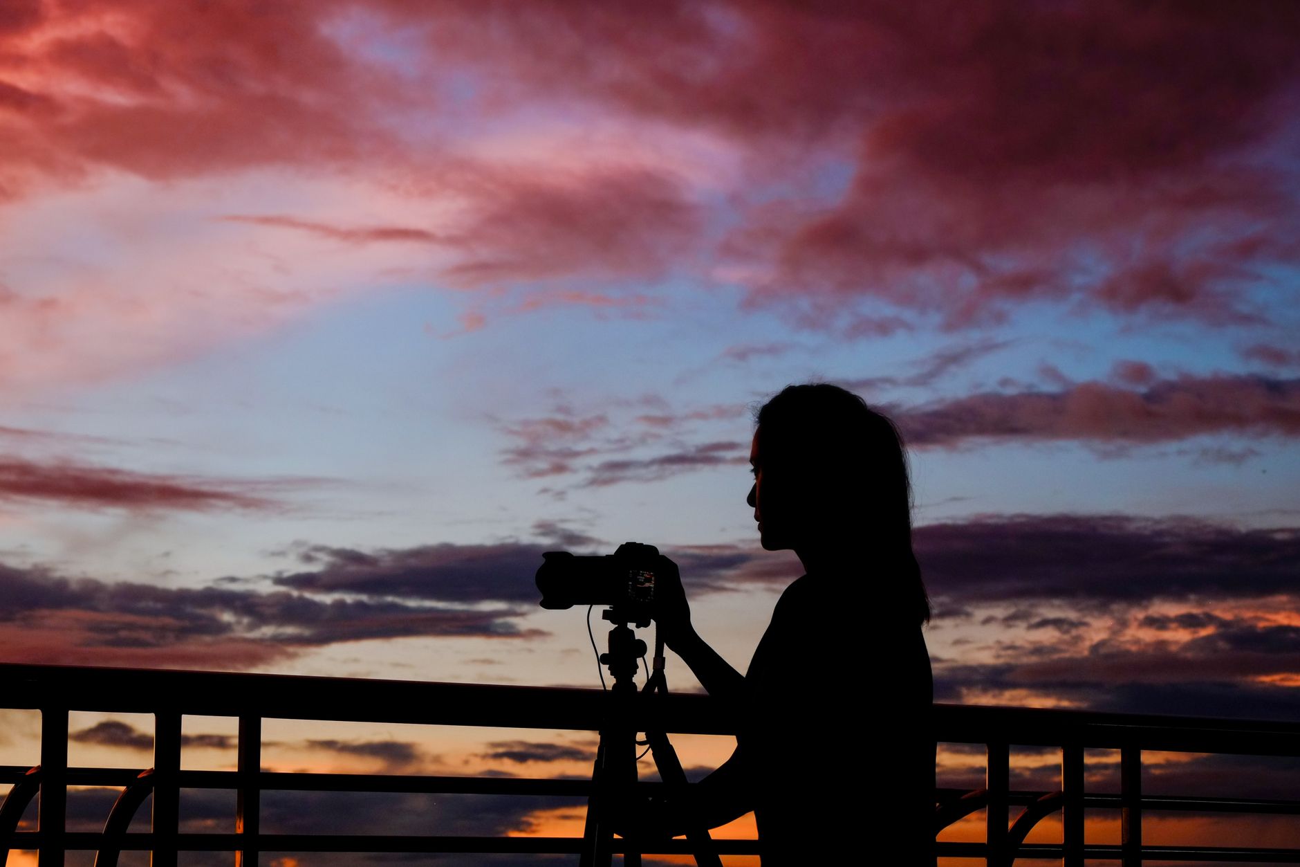 Sylwetka fotografki z aparatem na statywie na tle zachodu słońca
