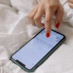 Jak rozpoznać fałszywy SMS od banku i nie stracić pieniędzy? Kobieta z czerwonymi paznokciami pisze na smartfonie w łóżku